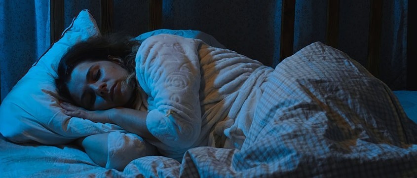 Vrouw ligt wakker in bed met hand op pijnlijke schouder door nachtelijke schouderklachten bij Fysiopark Uden