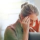 Vrouw achter laptop met handen tegen haar hoofd vanwege hoofdpijnklachten