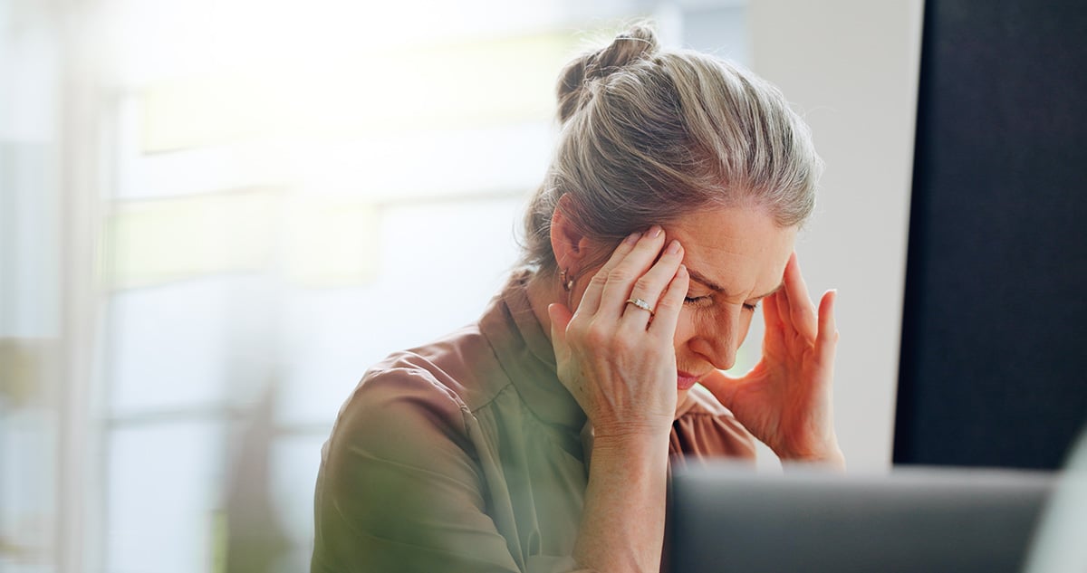 hoofdpijn-last-nek-hulp Vrouw achter laptop met handen tegen haar hoofd vanwege hoofdpijnklachten
